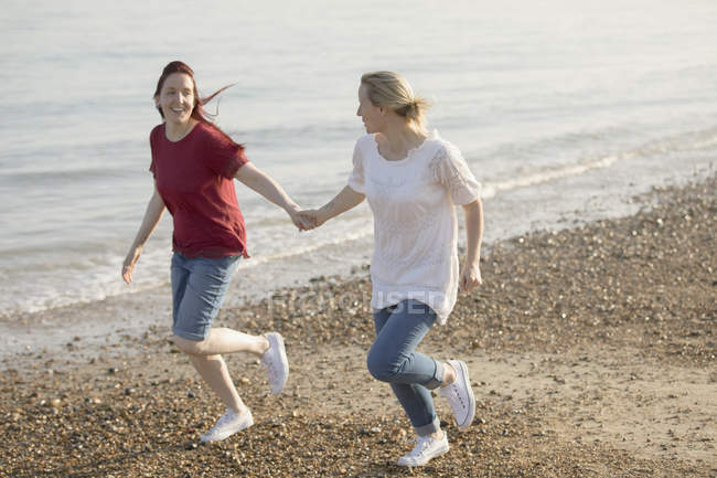 Verspieltes lesbisches Paar hält Händchen und rennt am sonnigen Strand — Stockfoto