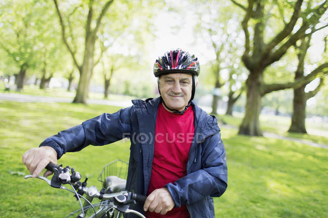 Portrait confident active senior man riding bike in park — Stock Photo