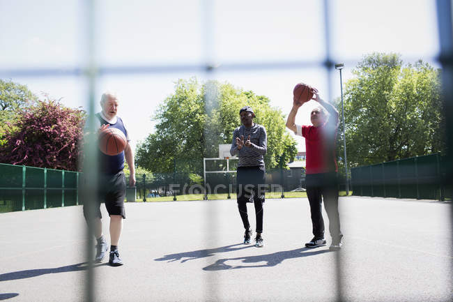 Homens seniores ativos jogando basquete no parque ensolarado — Fotografia de Stock
