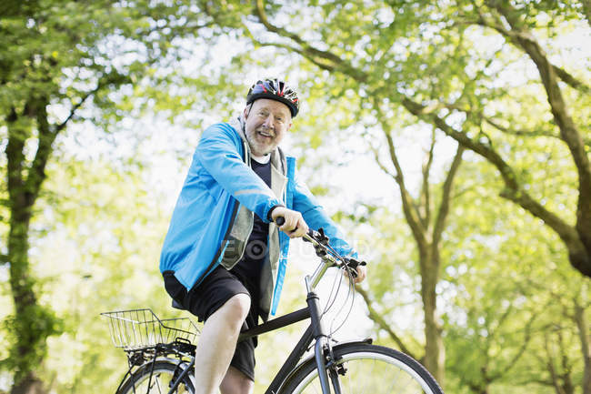 Retrato sorrindo ativo homem sênior andar de bicicleta no parque — Fotografia de Stock