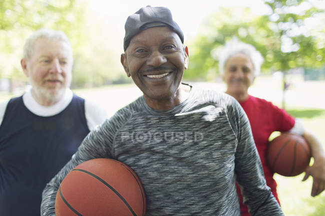 Retrato de confianza, sonriendo activos hombres mayores amigos con pelotas de baloncesto en el parque - foto de stock