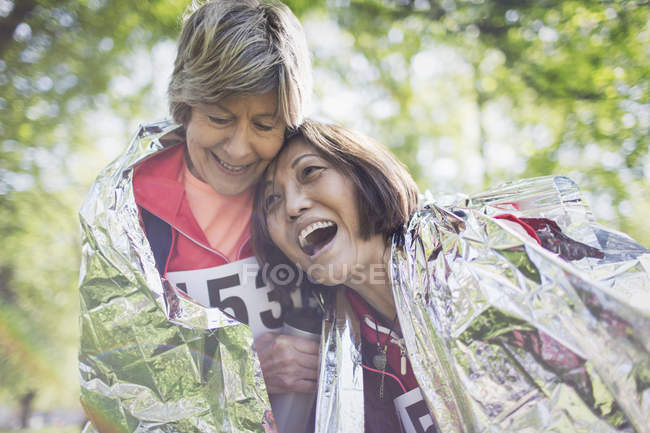 Felice attivo anziane donne amiche che si abbracciano dopo la gara sportiva, avvolto in una coperta termica — Foto stock