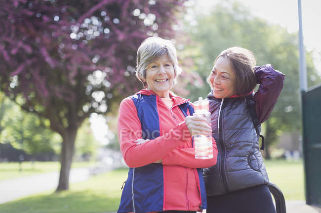 Portrait confident active senior female runner friends drinking water in park — Stock Photo