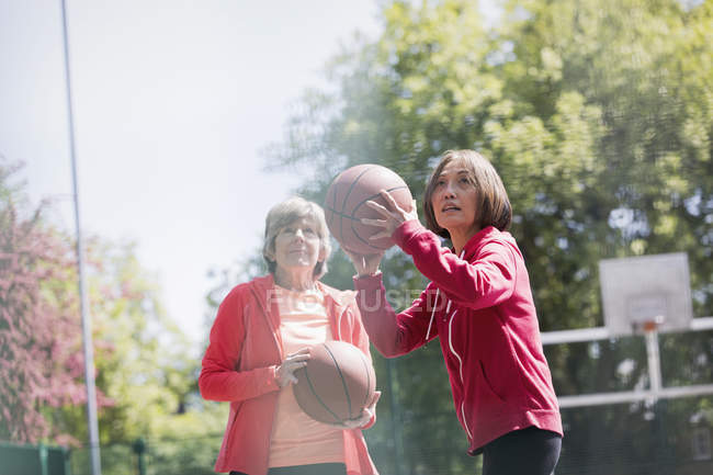 Mujeres mayores activas amigas jugando baloncesto en el soleado parque - foto de stock