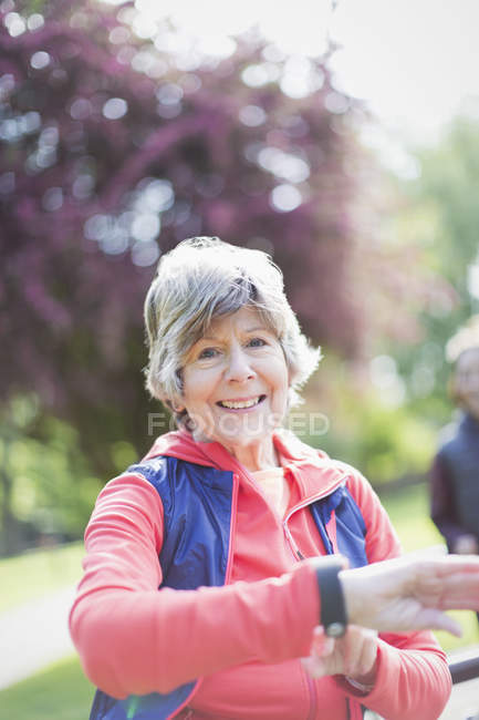 Portrait lächelnde, selbstbewusste, aktive Seniorin überprüft smarte Uhr im Park — Stockfoto