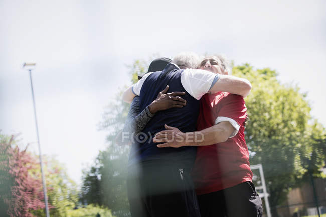 Hombres mayores activos amigos abrazándose en el soleado parque - foto de stock