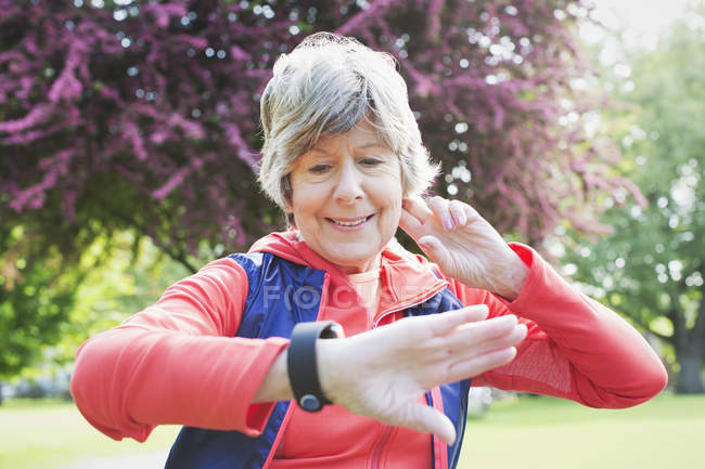 Активная старшая бегунья проверяет умные часы в парке — стоковое фото