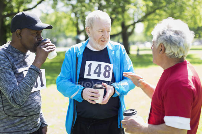 Homens seniores ativos amigos terminando corrida esportiva e beber café no parque ensolarado — Fotografia de Stock