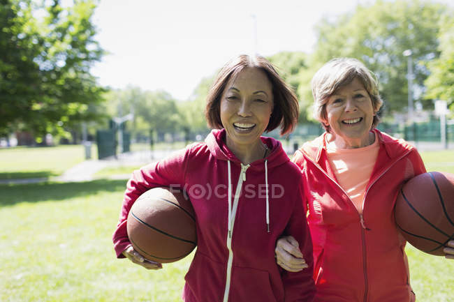 Retrato feliz, activo senior amigas jugando baloncesto en el soleado parque - foto de stock