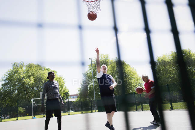 Активні літні чоловіки грають у баскетбол у сонячному парку — стокове фото