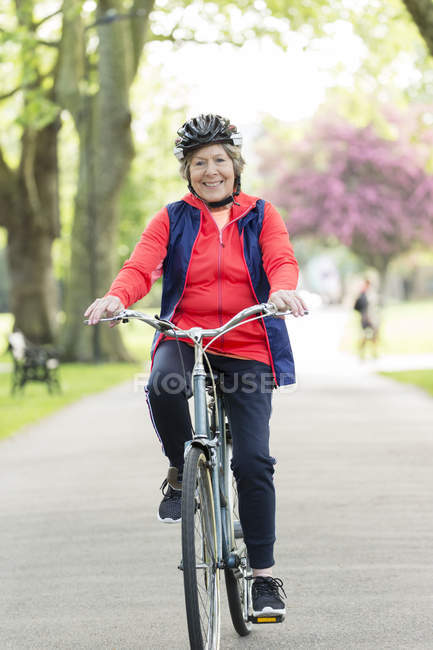 Retrato ativo sênior mulher andar de bicicleta no parque — Fotografia de Stock