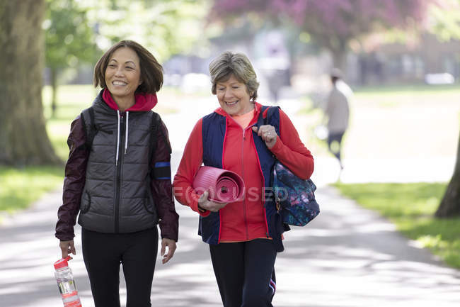 Active senior women friends with yoga mat walking in park — Stock Photo