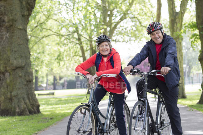 Portrait souriant, confiant couple de personnes âgées actives à vélo dans le parc — Photo de stock