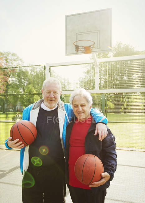 Portrait confident active senior men friends playing basketball in sunny park — Stock Photo