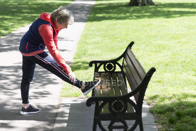 Активна старша жінка розтягує ногу на лавці парку — стокове фото