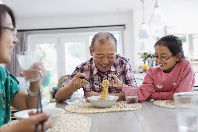 Grandfather and granddaughter sharing noodles at table — Stock Photo
