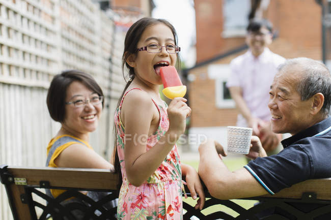 Portrait happy girl eating flavored ice with multi-generation family in back yard — Stock Photo