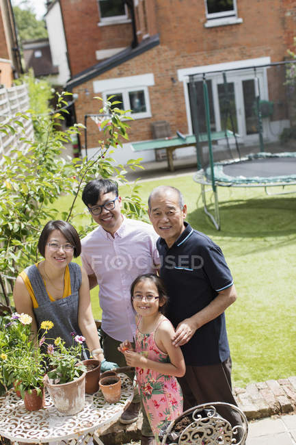 Retrato sonriente multi-generación jardinería familiar, flores macetas en patio soleado - foto de stock