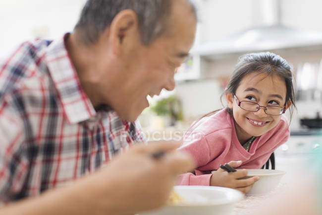 Усміхнений дідусь і онука їдять за столом — стокове фото
