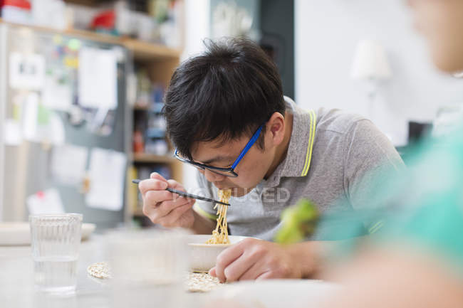 Человек ест лапшу с палочками за столом — стоковое фото