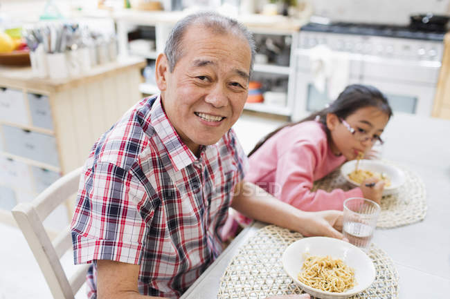 Retrato sorrindo avô comer macarrão com neta à mesa — Fotografia de Stock