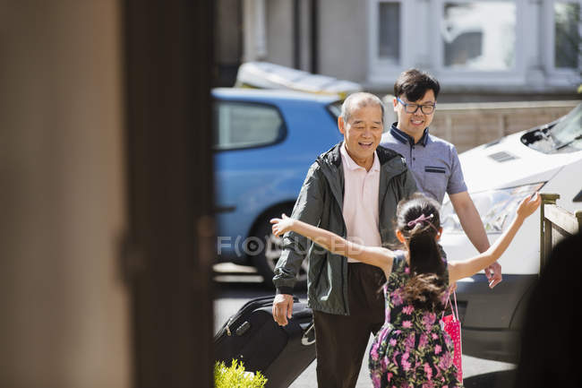Girl running to greet grandfather and father in sunny front yard — Stock Photo