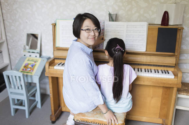 Portrait mère souriante assise avec sa fille jouant du piano — Photo de stock