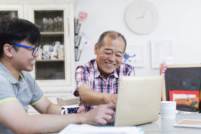 Son helping senior father using laptop in kitchen — Stock Photo