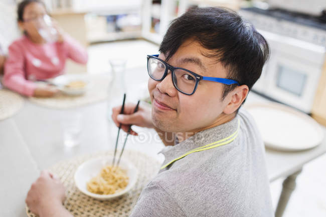 Porträt eines lächelnden Mannes, der am Tisch Nudeln mit Stäbchen isst — Stockfoto