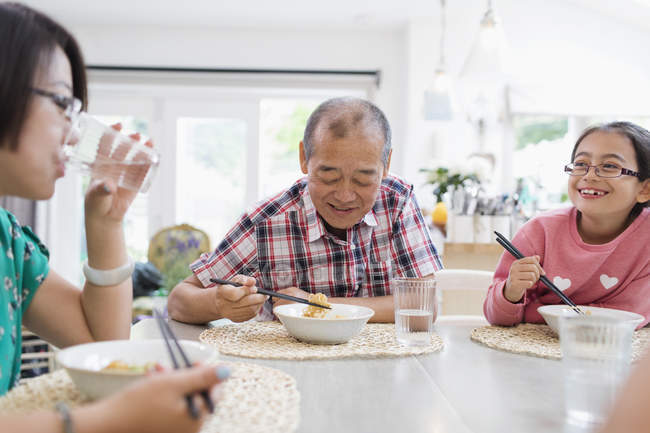 Familia multi-generación comiendo fideos con palillos en la mesa - foto de stock
