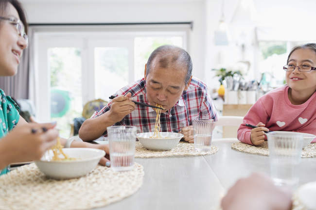 Родина багатьох поколінь їсть локшину з паличками за столом — стокове фото