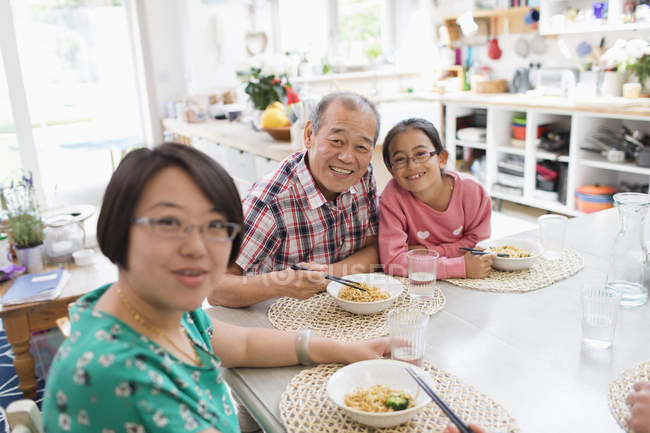 Retrato feliz familia multi-generación comiendo fideos con palillos en la mesa - foto de stock