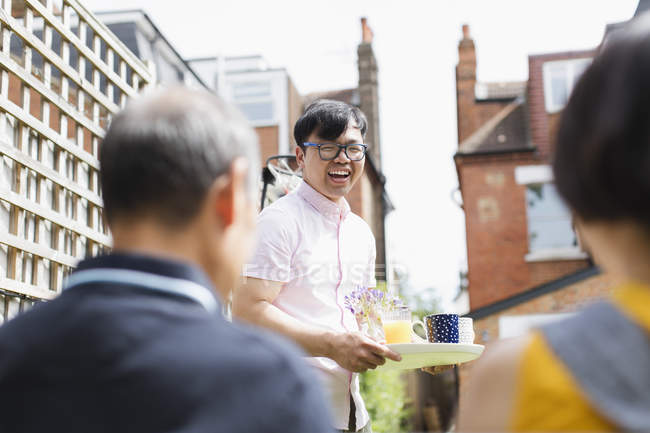 Счастливый мужчина угощает семью чаем и соком в солнечном дворе — стоковое фото