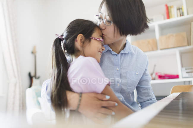 Affectionate mother and daughter hugging, playing piano — Stock Photo