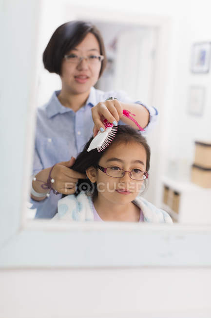 Madre cepillado hijas cabello en baño espejo - foto de stock