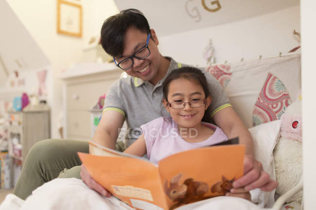 Padre e hija leyendo libro en el dormitorio - foto de stock