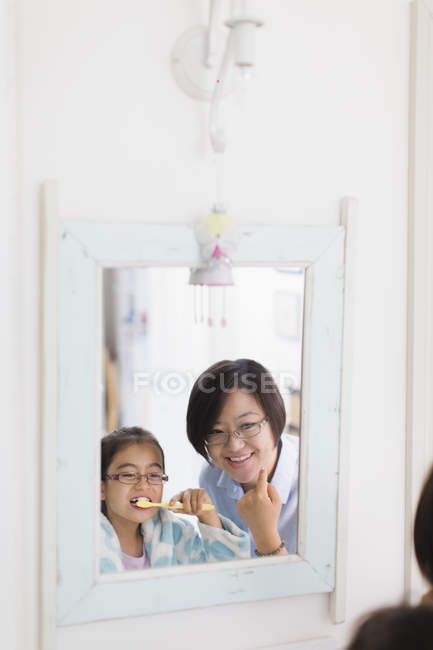 Mother watching daughter brushing teeth in bathroom mirror — Stock Photo