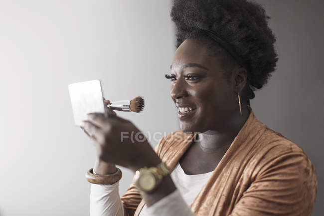 Smiling woman applying makeup in compact mirror — Stock Photo