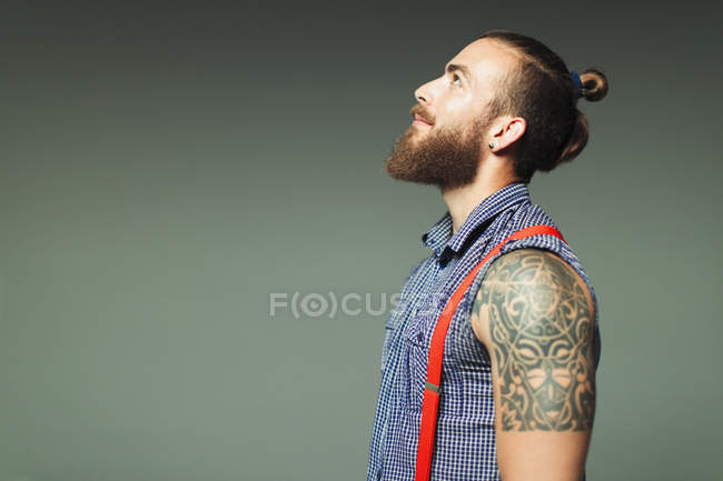 Curious hipster man with beard and shoulder tattoo looking up — Stock Photo