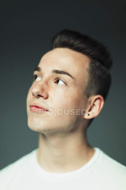Portrait thoughtful teenage boy with freckles and earring looking up — Stock Photo