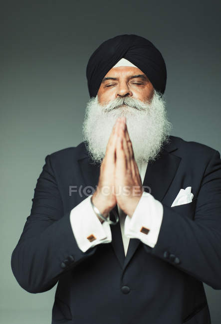 Retrato sereno hombre mayor en turbante rezando con los ojos cerrados - foto de stock