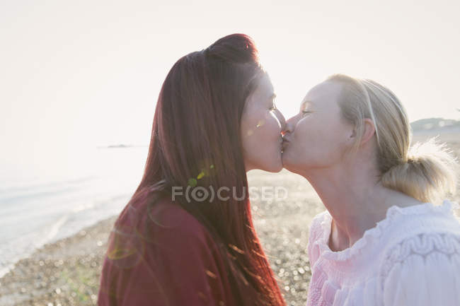 Casal lésbico afetuoso beijando na praia ensolarada — Fotografia de Stock