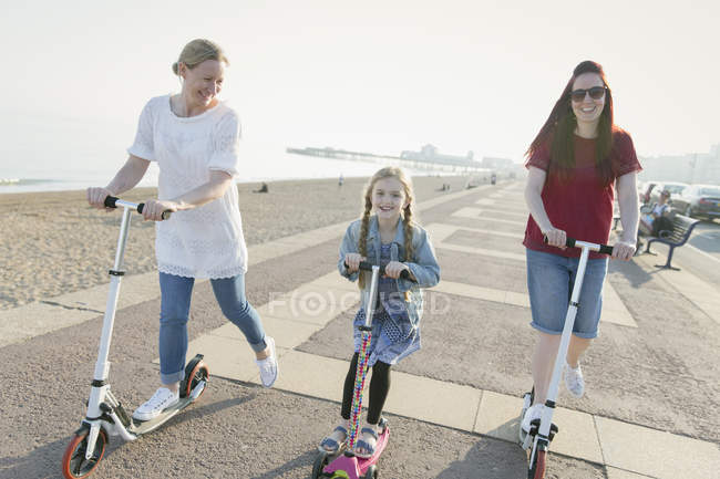 Coppia lesbica e figlia a cavallo spingere scooter sulla spiaggia soleggiata — Foto stock