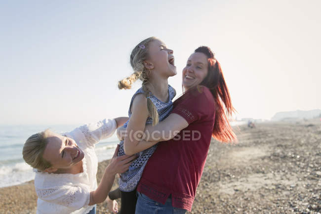 Pareja lesbiana y su hija riendo en la playa soleada - foto de stock