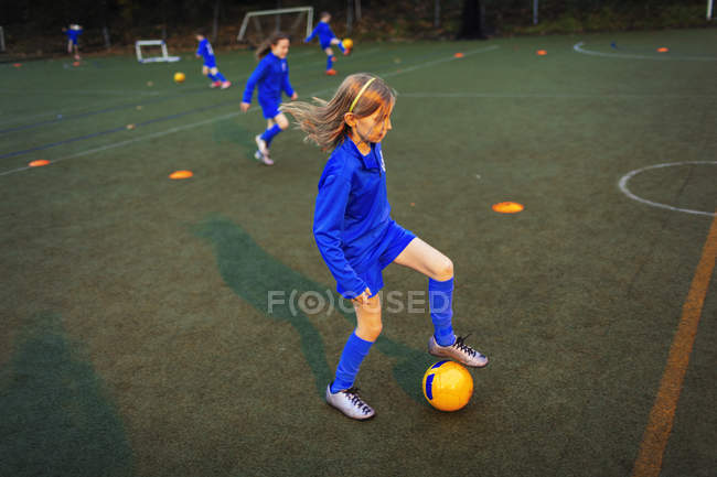 Chica practicando fútbol en el campo por la noche - foto de stock