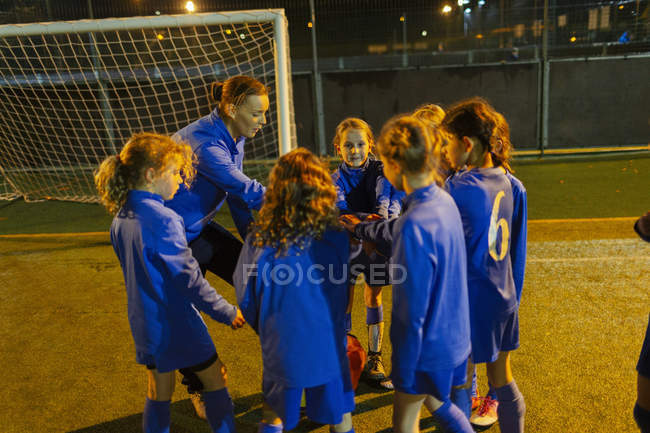 Allenatore di calcio e ragazze squadra di calcio in huddle sul campo di notte — Foto stock