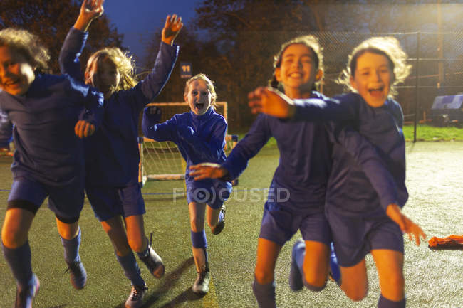Enthusiastic girls soccer team running and celebrating on field at night — Stock Photo