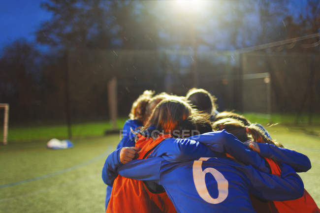 Girls soccer team huddling on field at night — Stock Photo