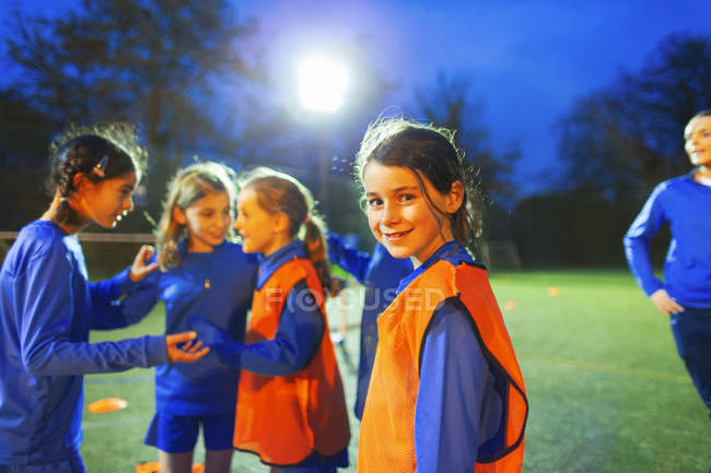 Портрет уверенной девушки футболистки на поле с командой ночью — стоковое фото