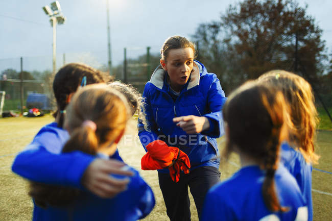 Chicas equipo de fútbol escuchando entrenador en el campo por la noche - foto de stock